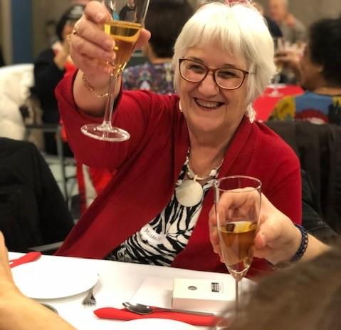 Smiling white haired woman wearing bright red sweater holding glass up for cheers